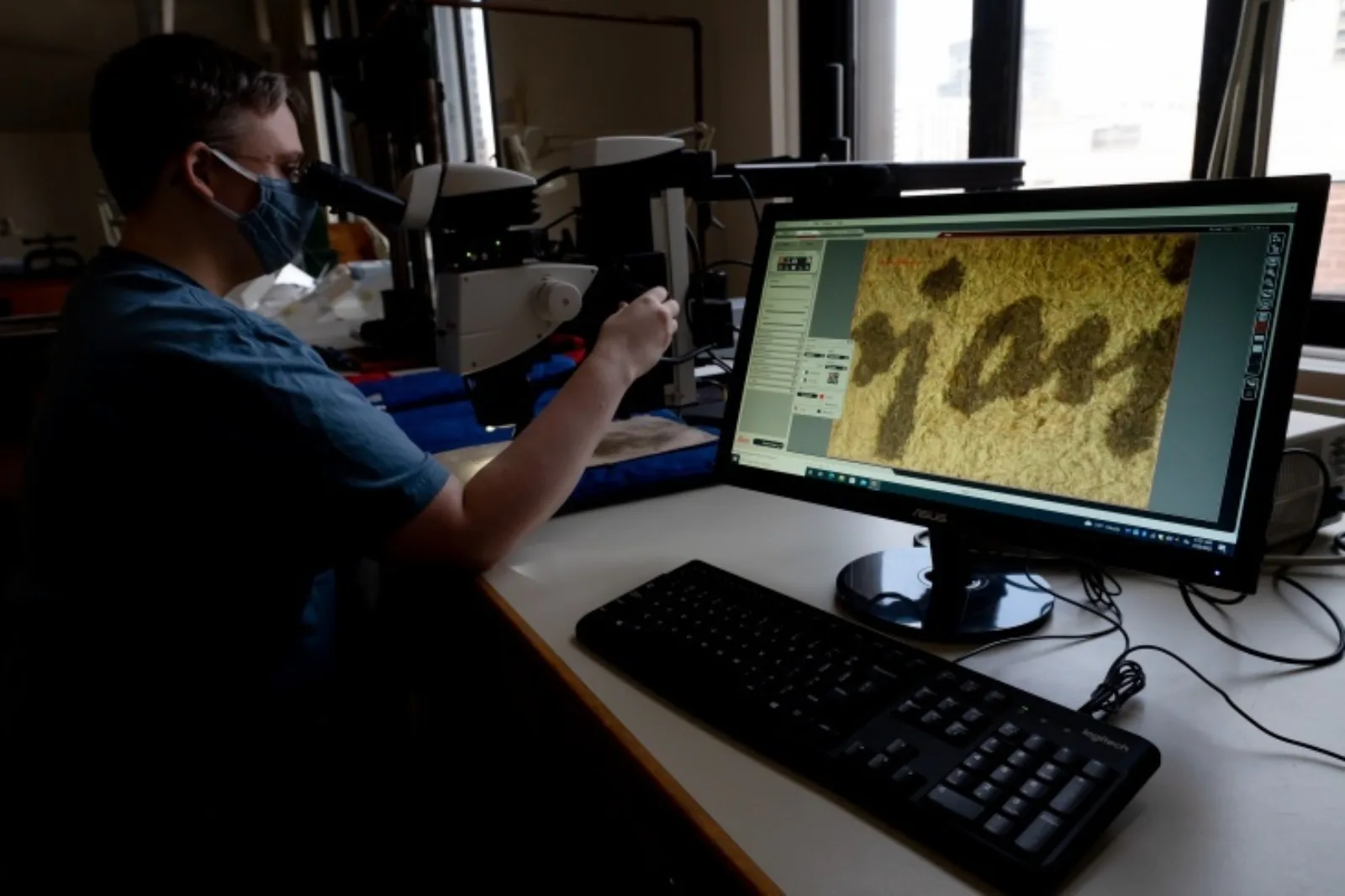 Leith working in the conservation lab Leith is looking at Ayer 1485 through a powerful microscope. On the right is a computer monitor that displays the view of the microscope.