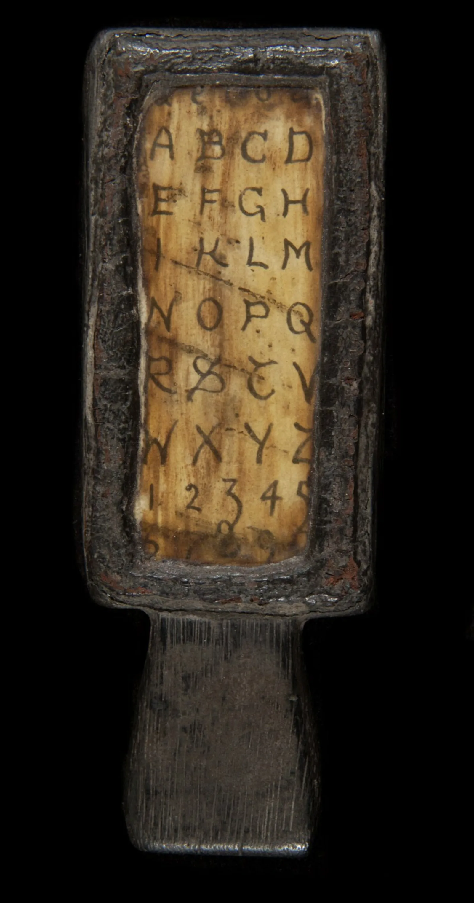 A hornbook A small wooden paddle has a transparent screen running vertically. Under the screen is a handwritten alphabet.