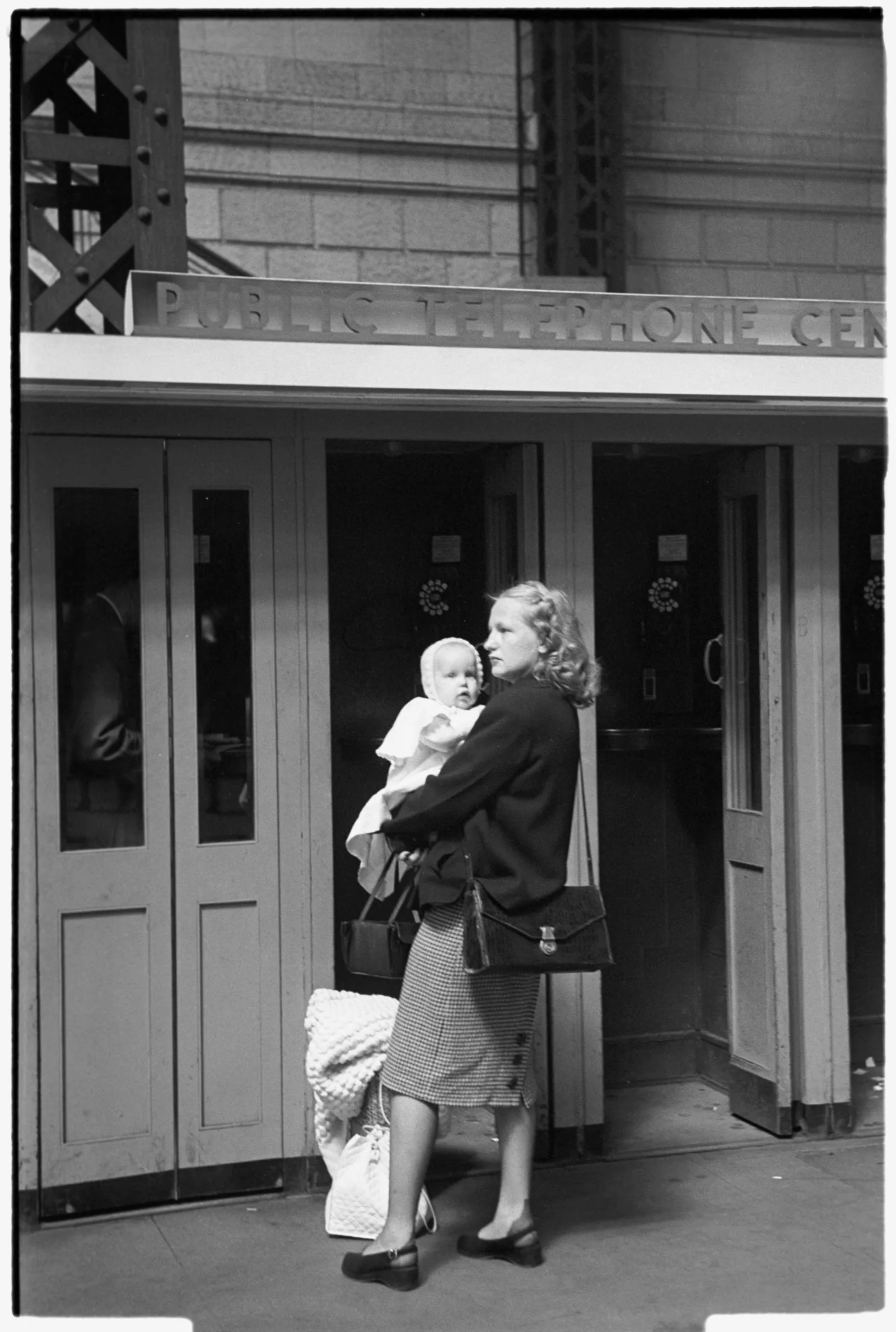 CBQGR118 A mother holding her infant child in front of a row of train station telephone booths