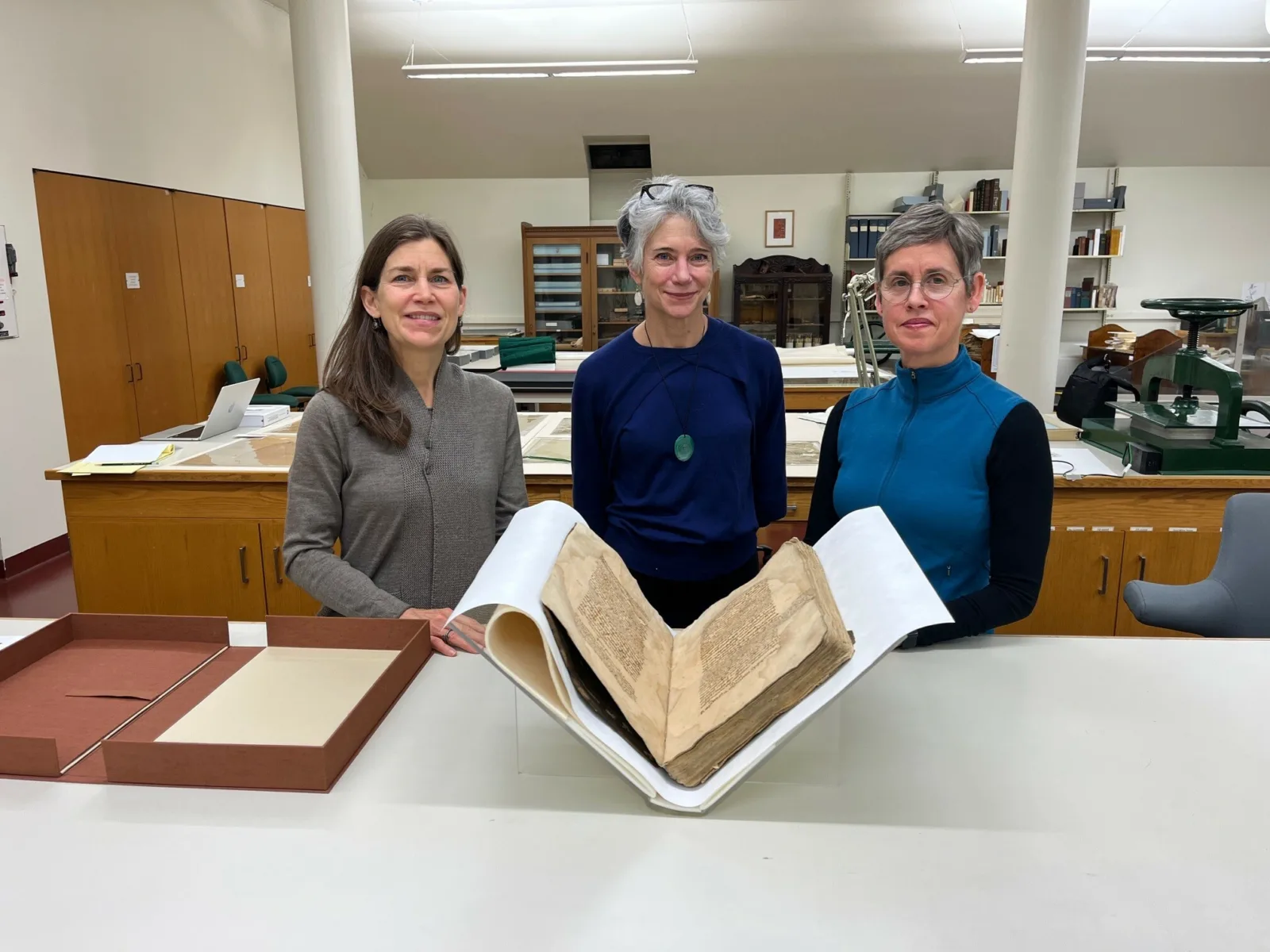 With Maguey Paper Three people stand with a large bound manuscript in the foreground.