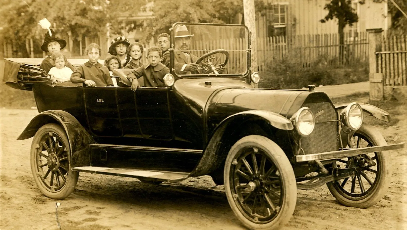 MMS Prescott 015 Automobile portrait 1913 The Lyons family in their car, 1913. From L-R and relation to Eunice: Eva Sybil Carrington Lyons (mother), Eva Gwendolyn Lyons (sister), Eunice Lavinia Lyons, Emma A. Lyons (sister), Louise Lyons (sister), Maxine Moore (cousin), Woodward Cecil “Joe” Lyons (brother), Wendell C “Big Brother” Lyons (brother), L.D. Lyons (father).