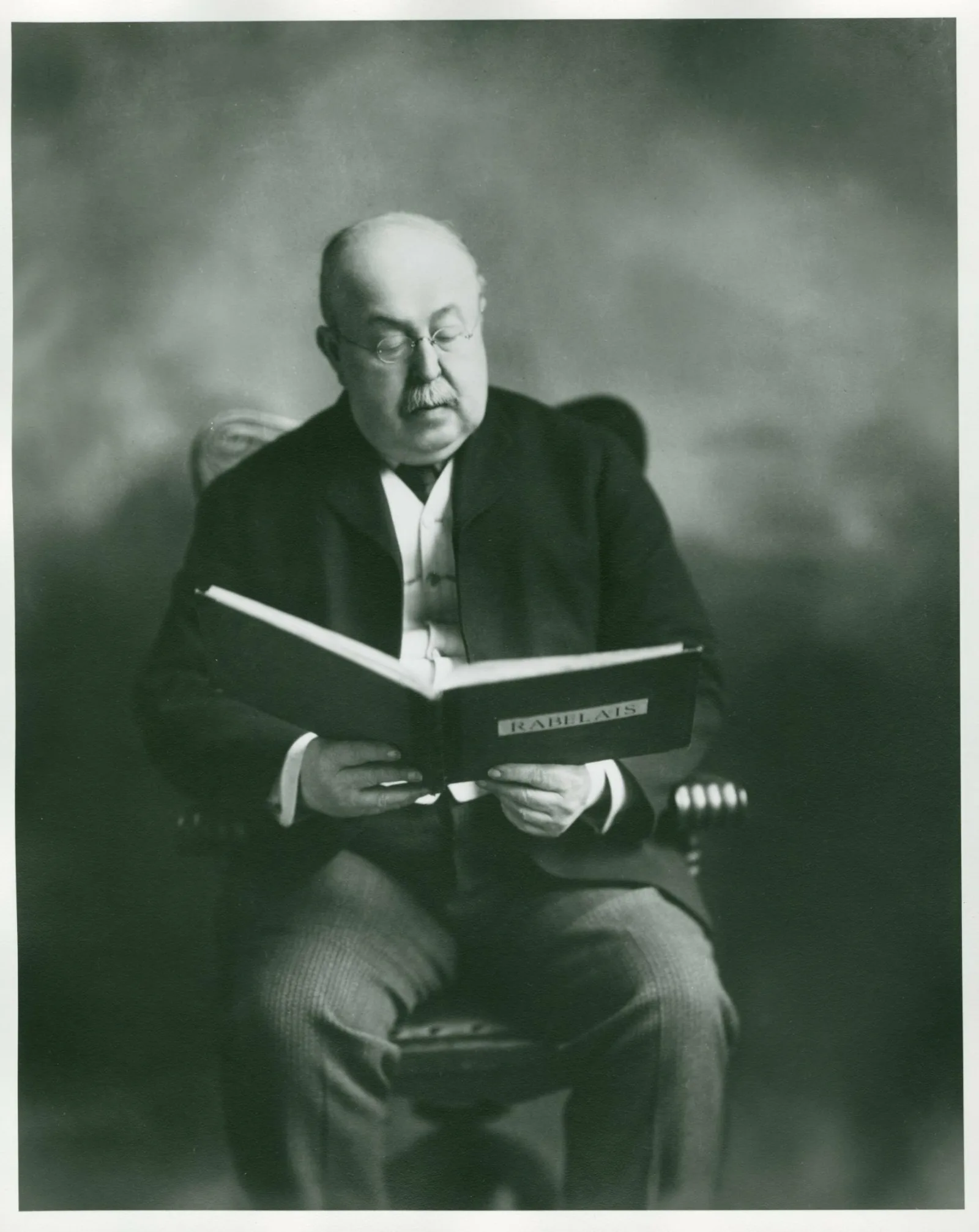 John M. Wing An older man sits in a chair reading.