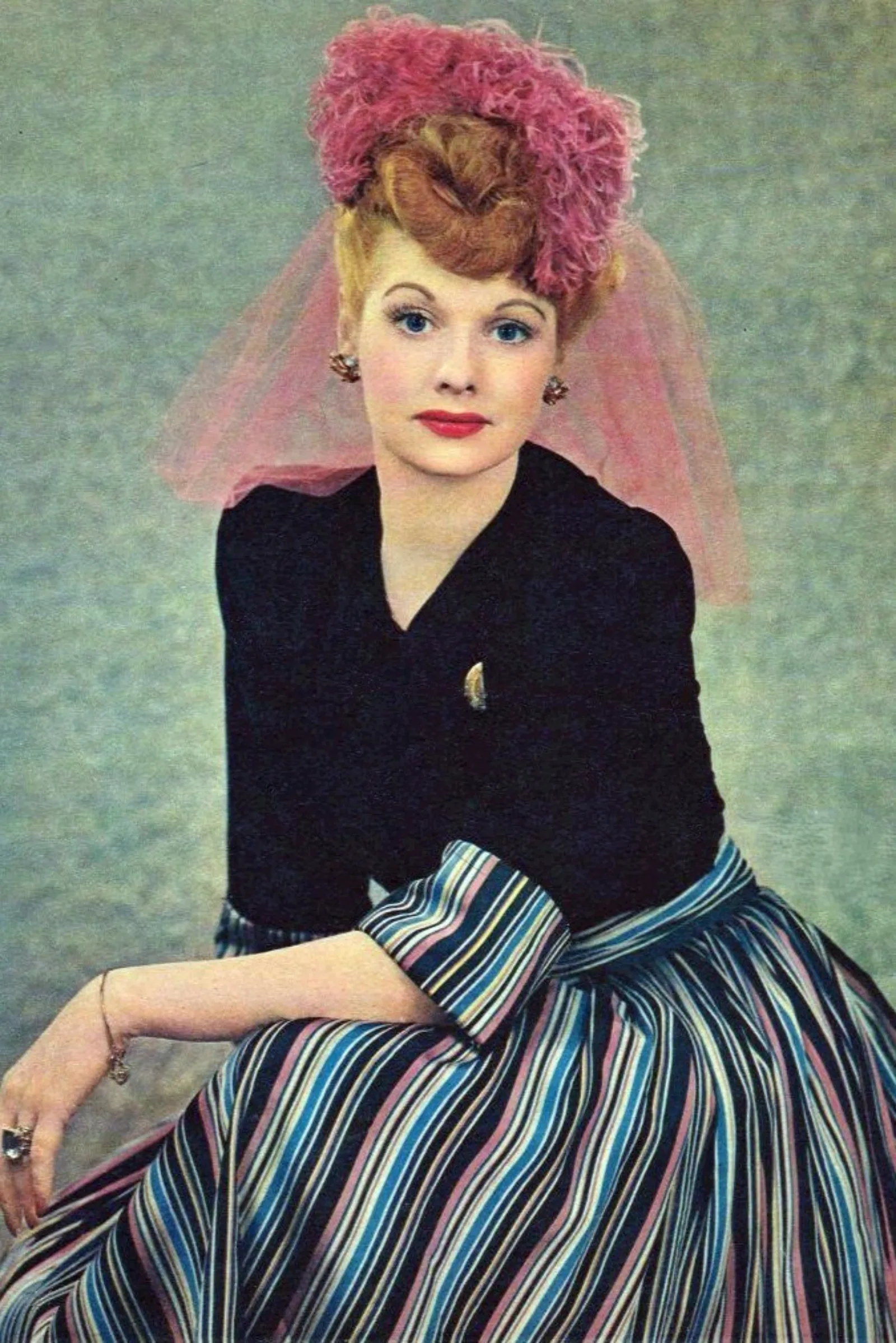 A vibrant photograph of Lucille Ball against a green background. She is wearing a pink hat and a dress with multi-colored stripes.